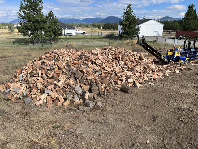 Wide pile of split firewood with the processor parked at the far end
